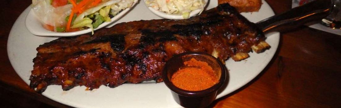A picture of pork back ribs with coleslaw and salad on the side.