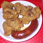 A picture of some deep-fried chicken liver pieces and a fried sausage on a plate.